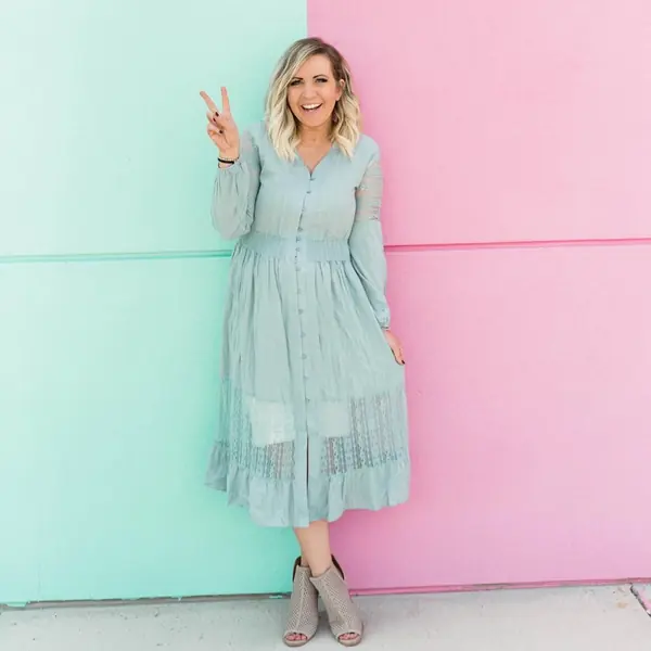 Dani, founder of the Bestie Squad, in a sage midi dress giving a peace sign in front of a teal and pink wall.