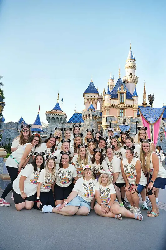 A group of Bestie Squad women smiling in front of a fairytale castle at a theme park.